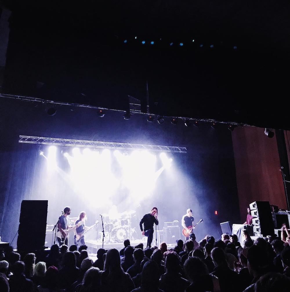 The band Deafheaven performs on stage, with a large crowd of people watching. 