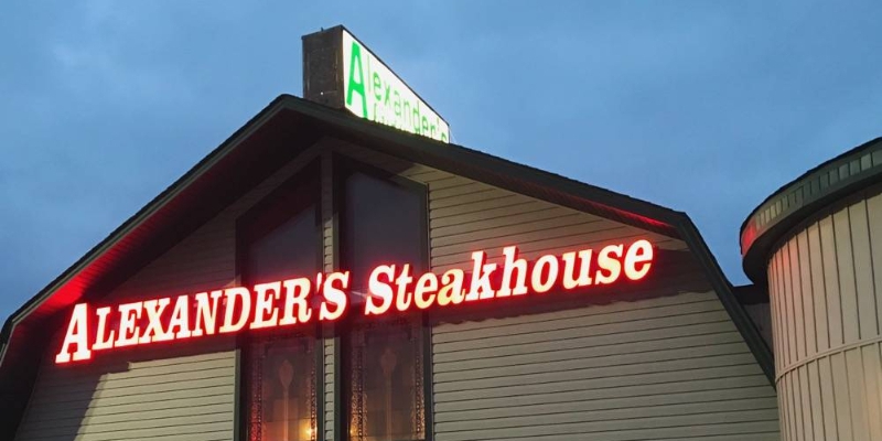 The exterior of Alexander's Steakhouse, featuring their neon signage lit up