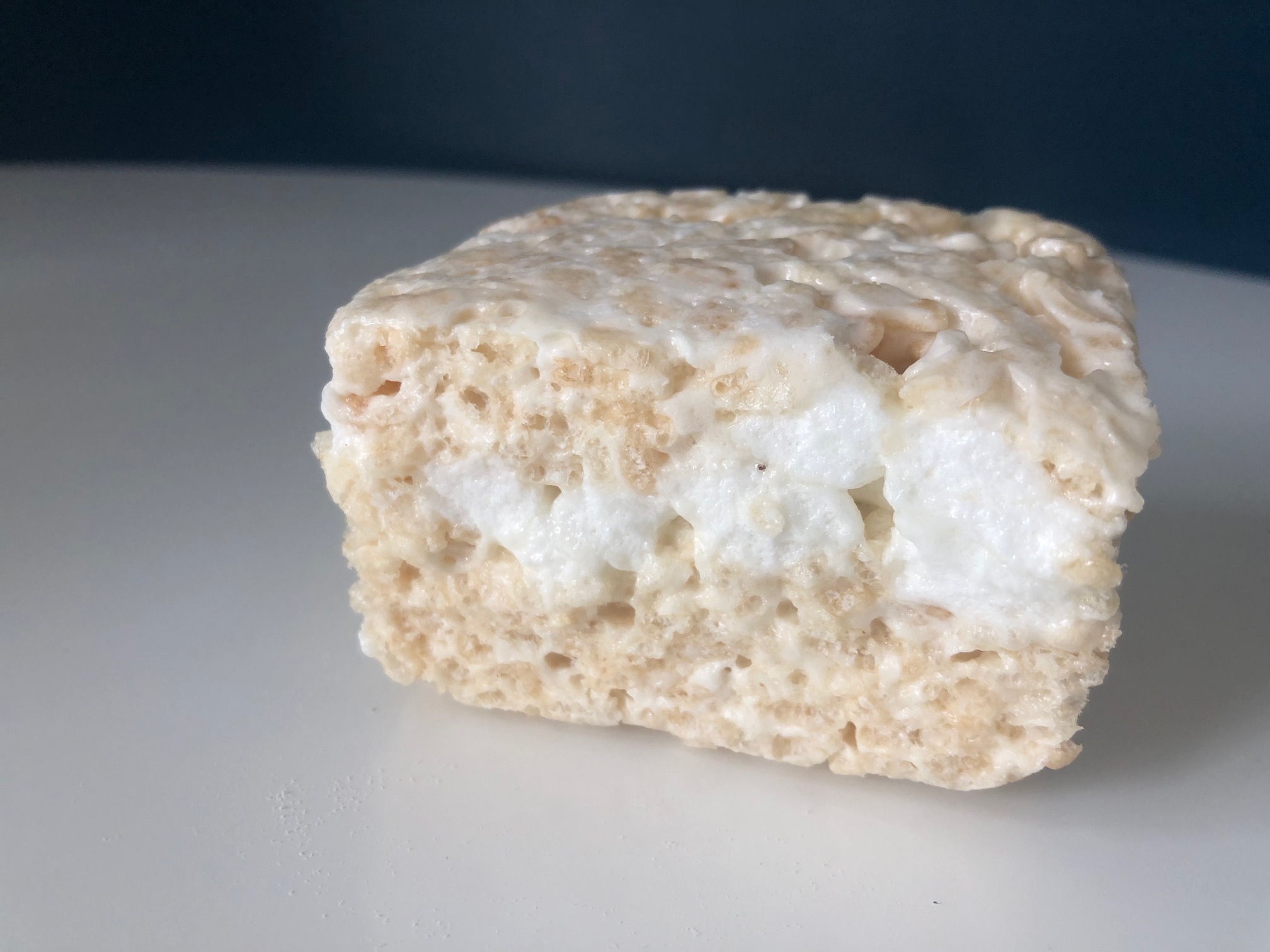 On a white plate, there is a brick of rice krispie treat with visible mini marshmallows. Photo by Alyssa Buckley.