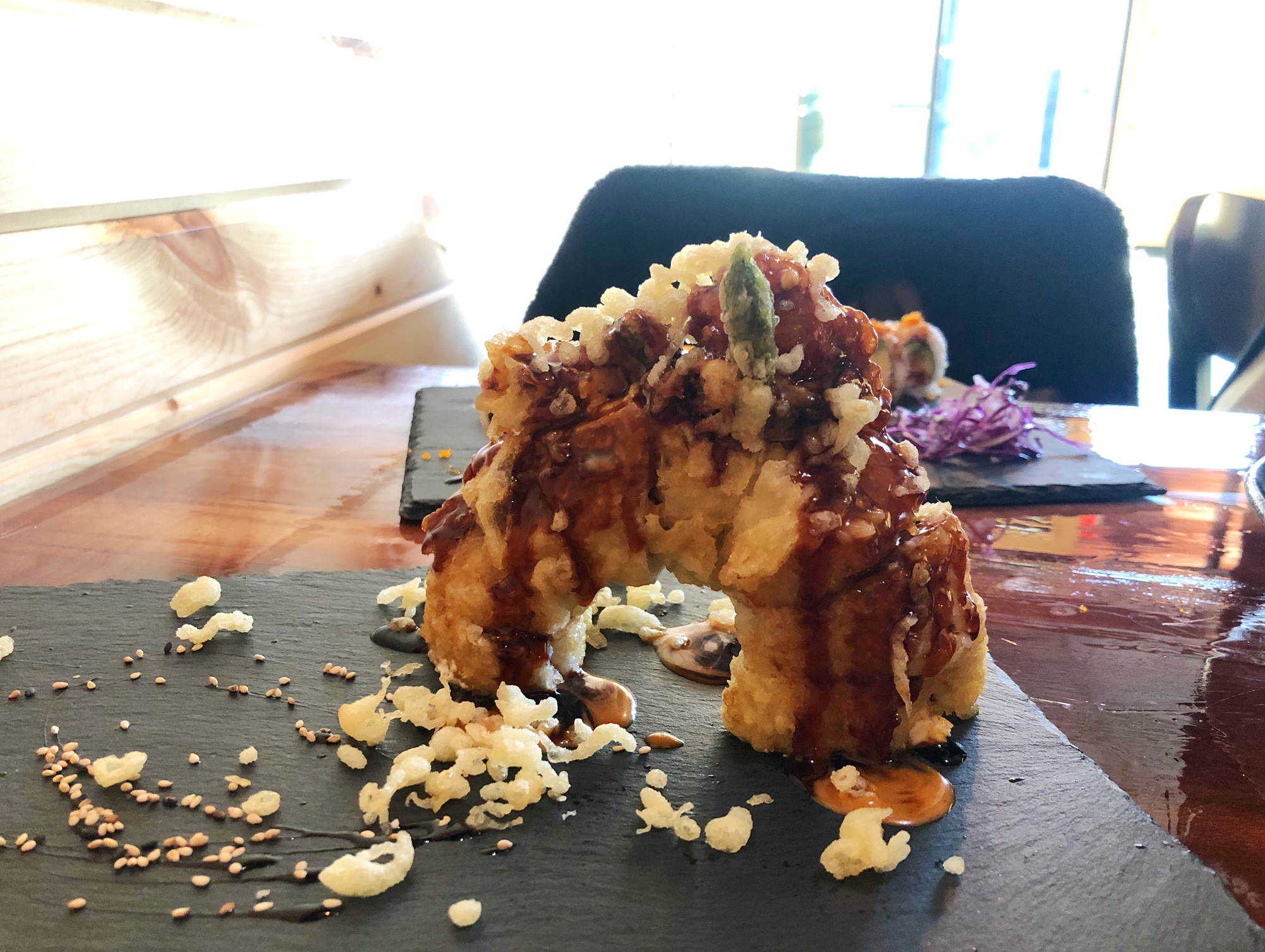 On a black stone tray, there is a sushi roll that has been fried and covered in tempura crunchies with eel sauce. Photo by Alyssa Buckley.