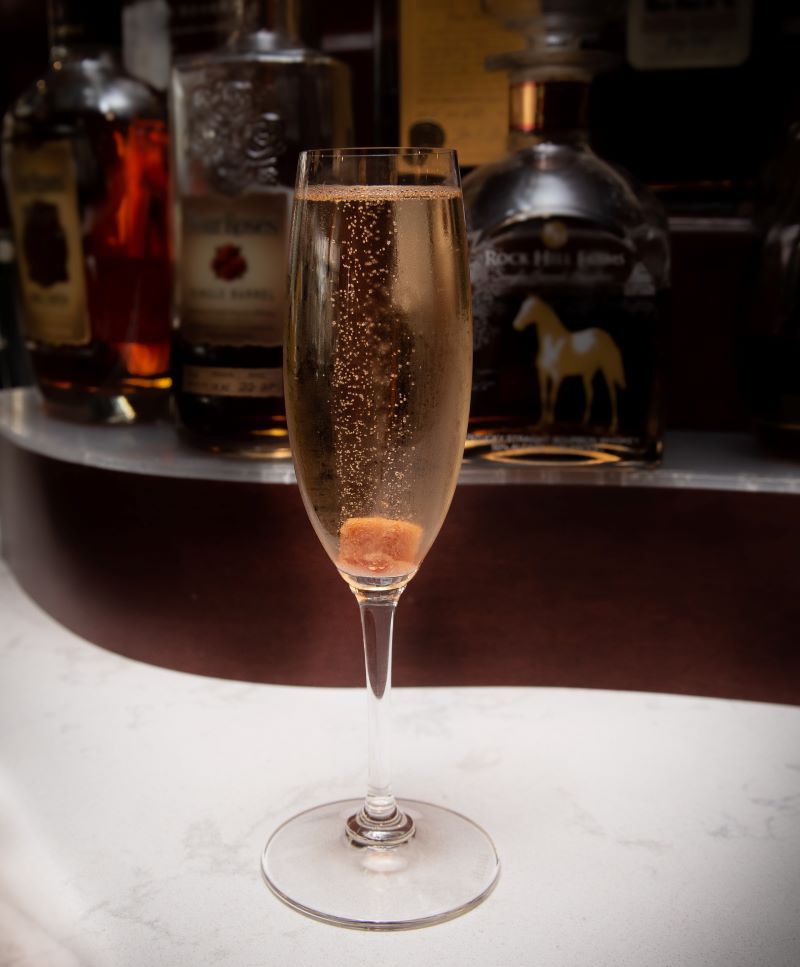 A champagne flute with bubbling champagne and a brown sugar cube in the bottom is sitting on a white marble bar. Photo from Hamilton Walker's.