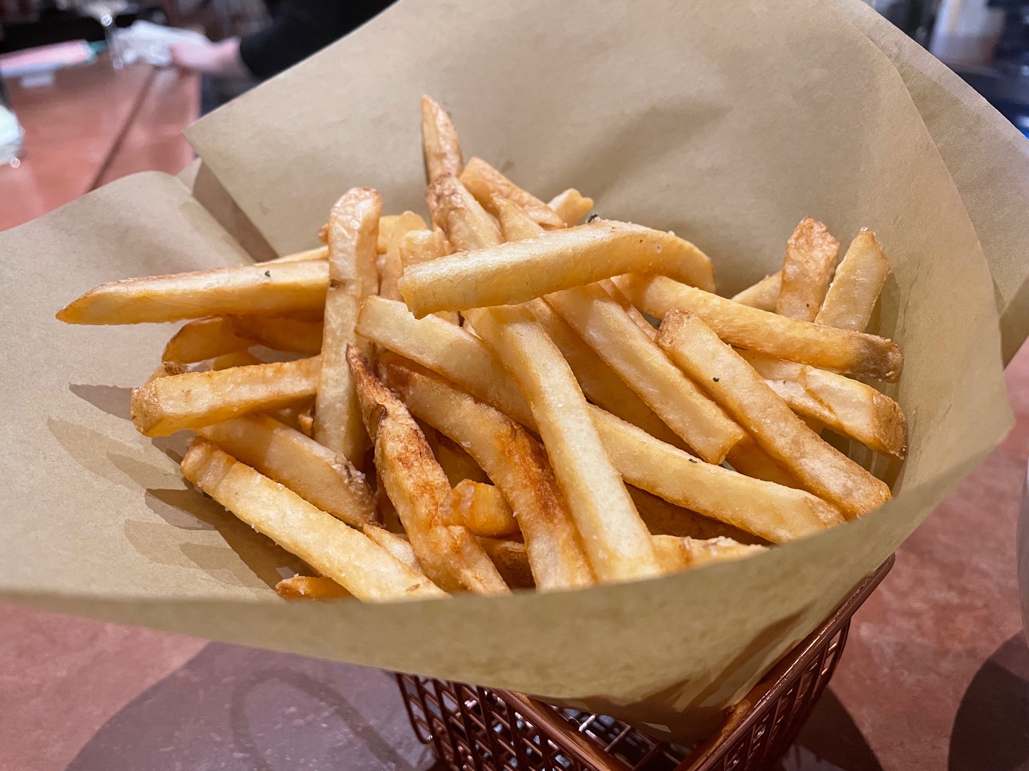 In a rose gold basket, there is a portion of fries on brown parchment paper. Photo by Alyssa Buckley.