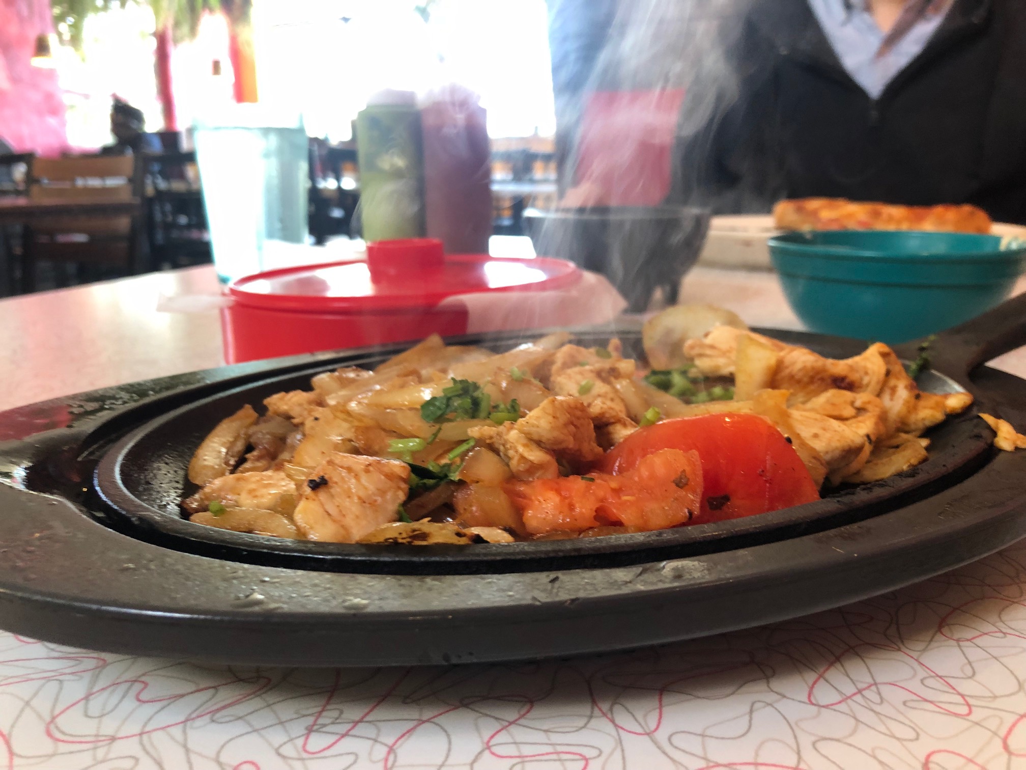 On a retro table, there is a fajita skillet with chicken, onions, tomato, and cilantro on top. There is steam coming off the top. Photo by Alyssa Buckley.