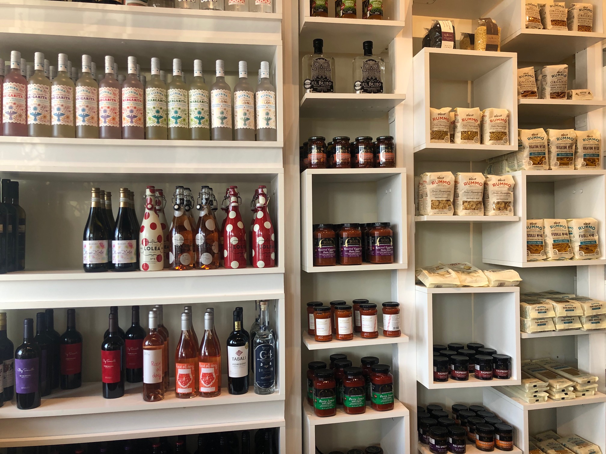 On white shelves, bottles of wine, bottles of sauce, and dry pasta in bags neatly line the shelves. Photo by Alyssa Buckley.