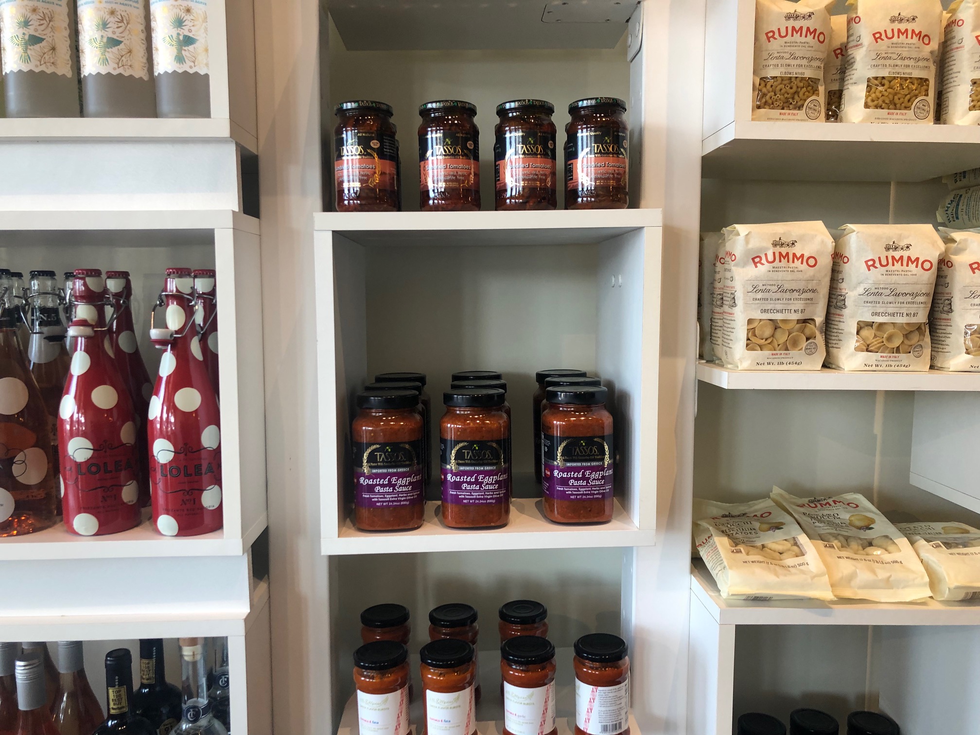 White shelves are neatly stocked with dry pasta in bags and jarred red sauce. Photo by Alyssa Buckley.