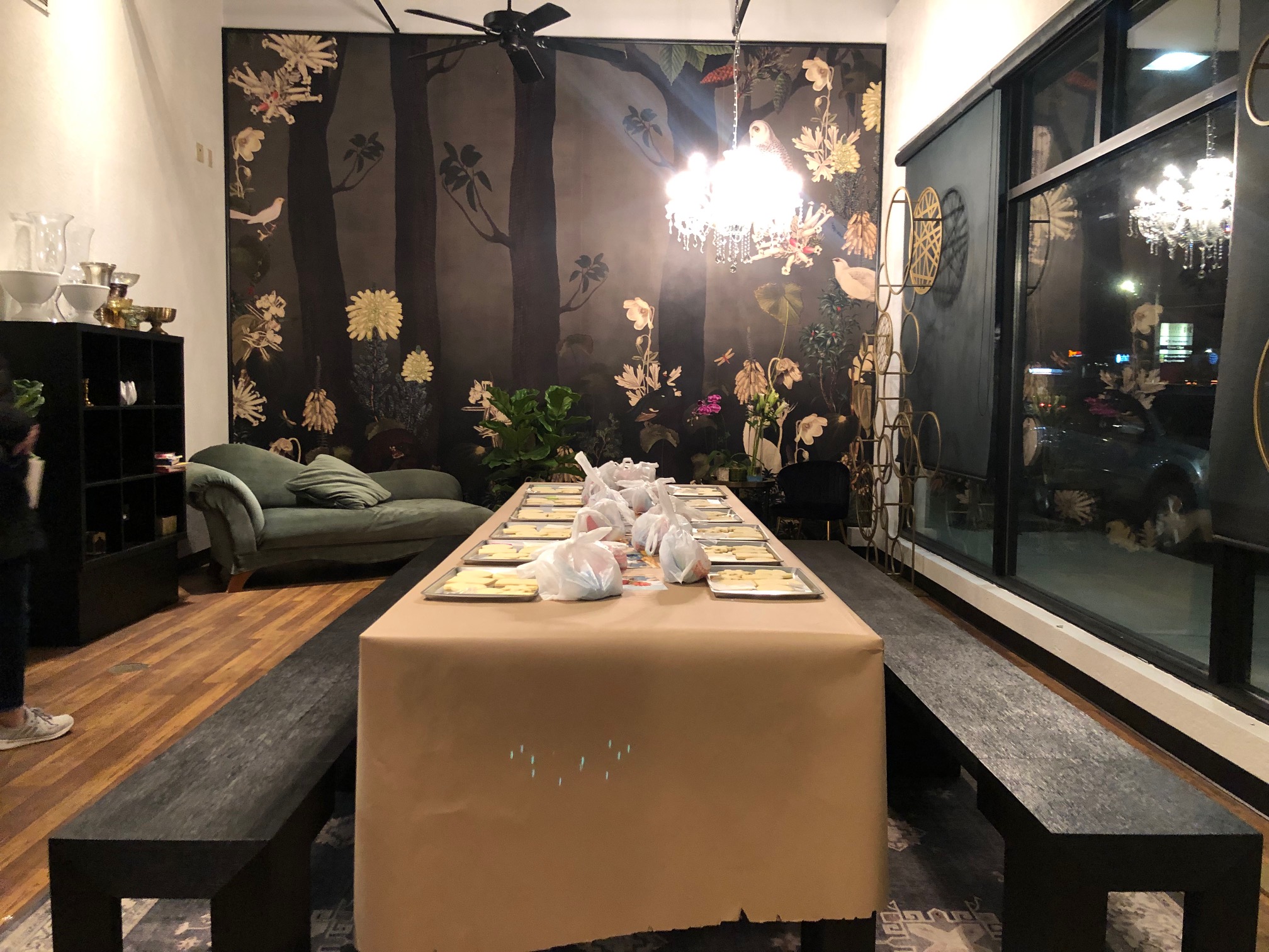 Two long black benches are pulled up to a long table with a brown craft paper table cover. There is a feature wall behind that is black with flowers. Photo by Alyssa Buckley.