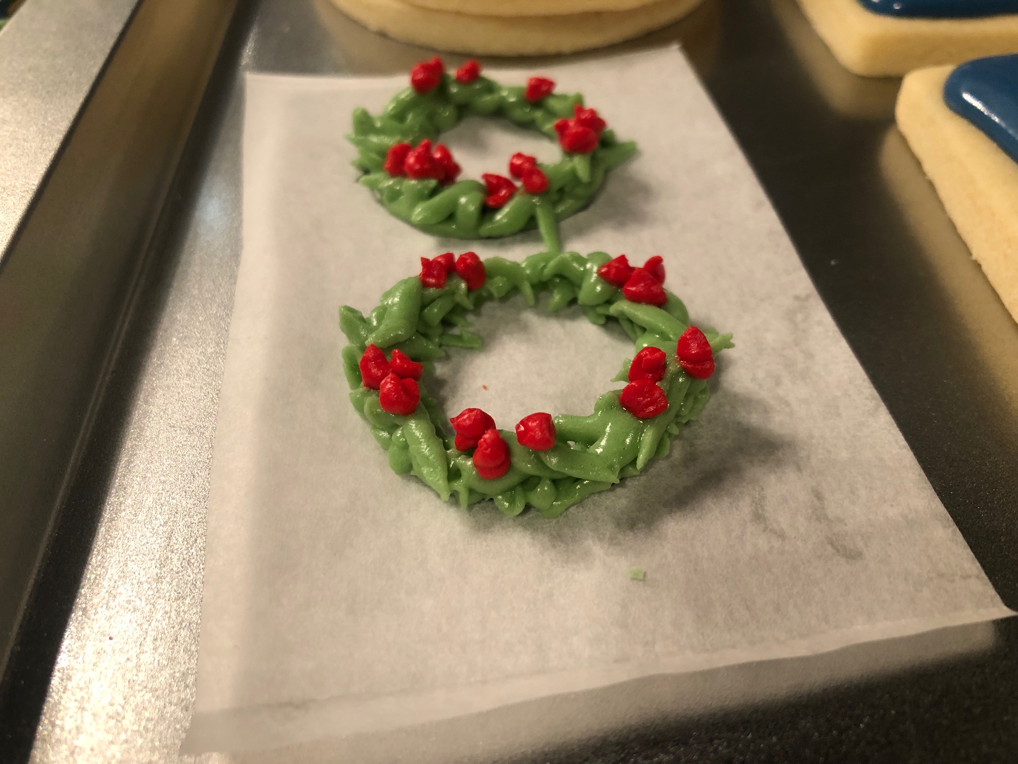 On a metal pan, two wreaths made out of icing with red circles sit on parchment paper. Photo by Alyssa Buckley.