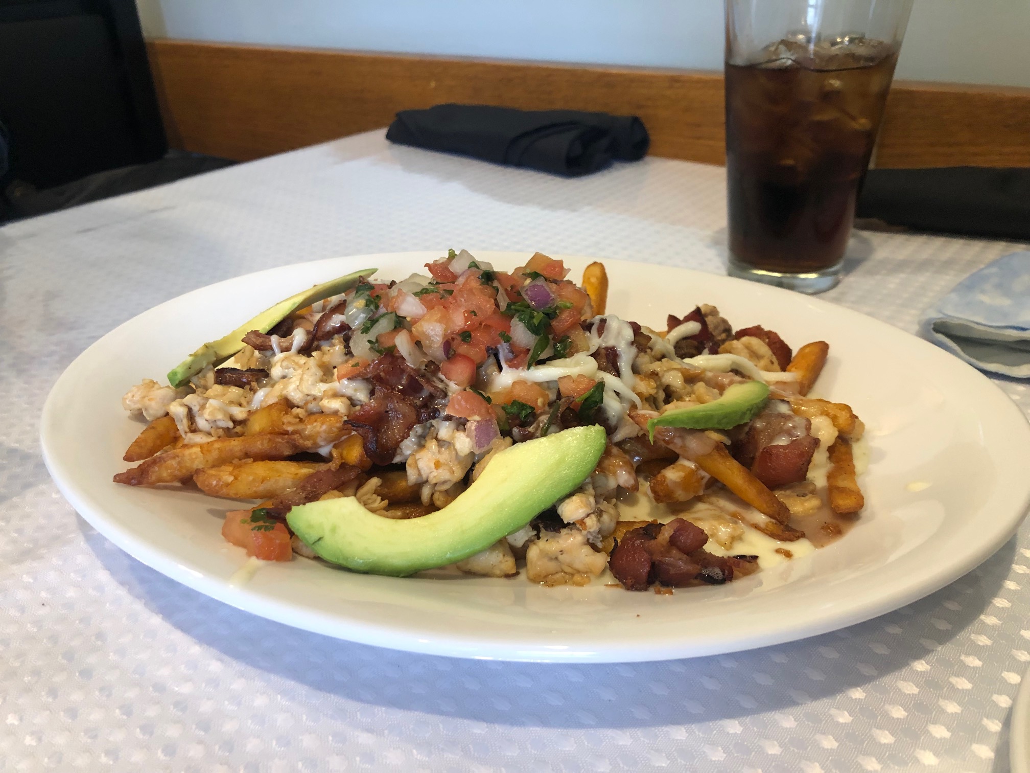 On a white plate, there is a bed of fries with cheese and sliced avocado. Photo by Alyssa Buckley.