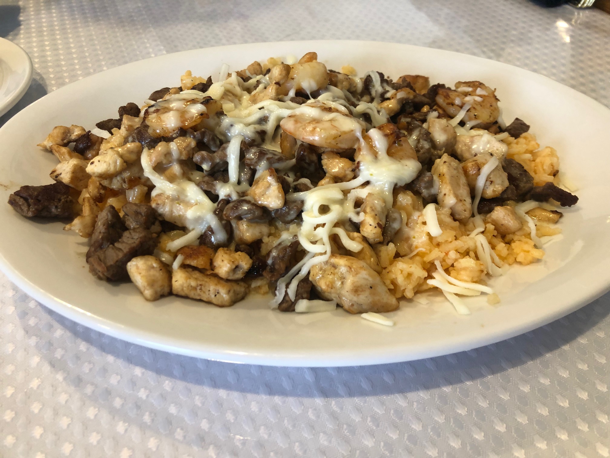 On a large white plate, there is a bed of rice covered in white cheese sauce with chicken, steak, and shrimp. Photo by Alyssa Buckley.