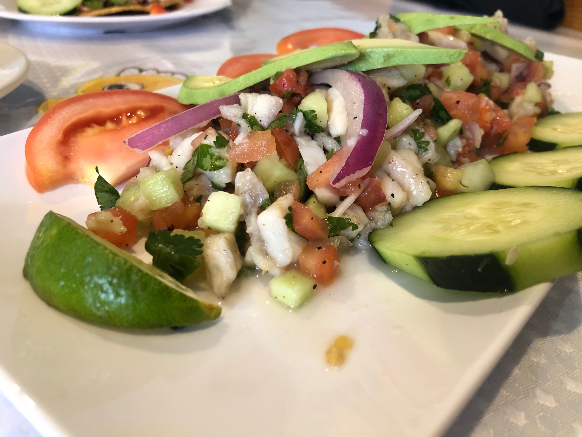 On a white plate, there is ceviche with white fish, limes, sliced cucumbers, and diced veggies. Photo by Alyssa Buckley.