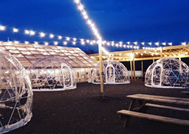 A beer garden with a greenhouse and four clear domes. There are string lights across the top of the space. Photo from Big Thorn Farm Facebook page.