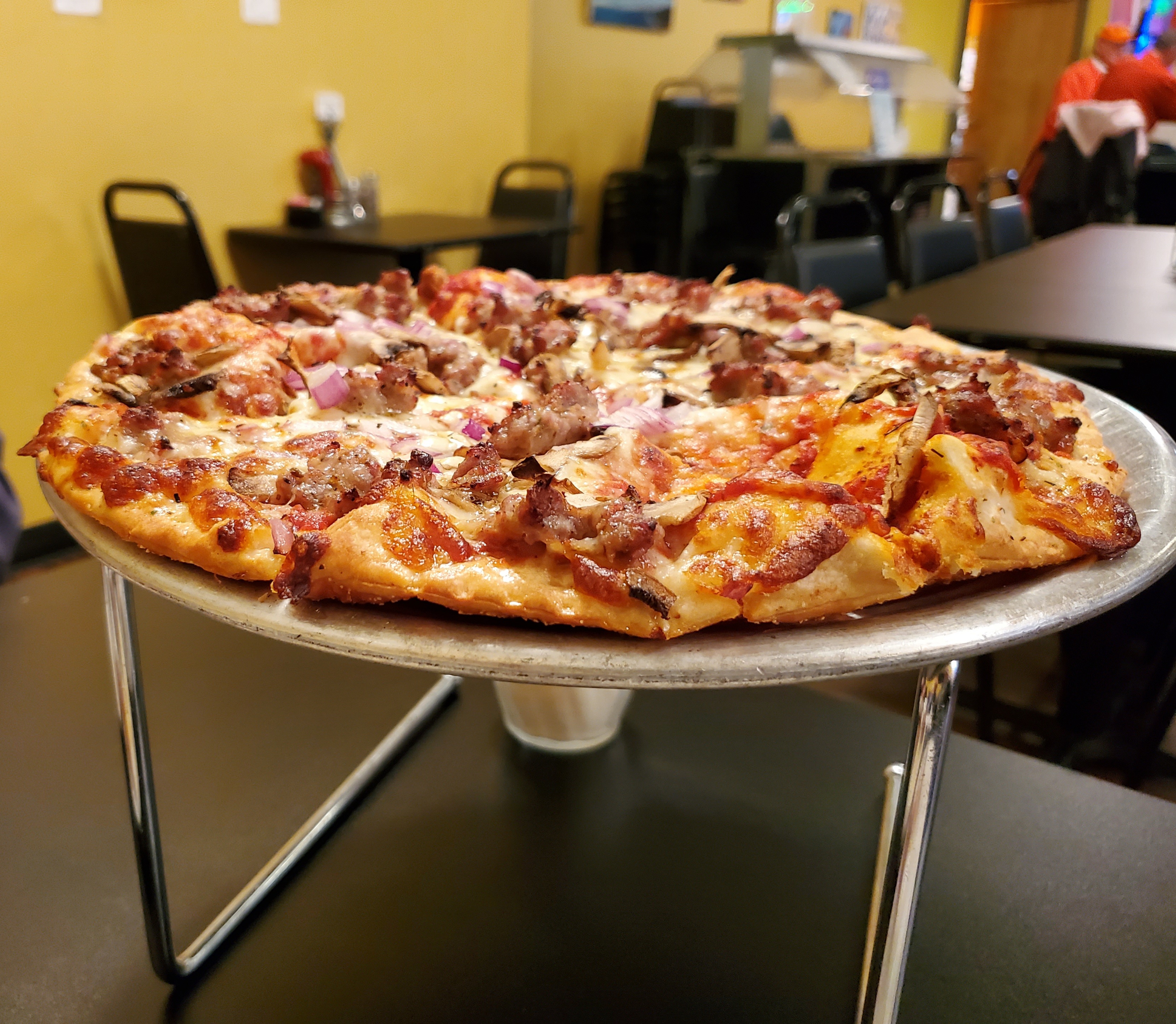 On a gray table, there is a pizza holder with a thin crust pizza sliced. Photo by Carl Busch.