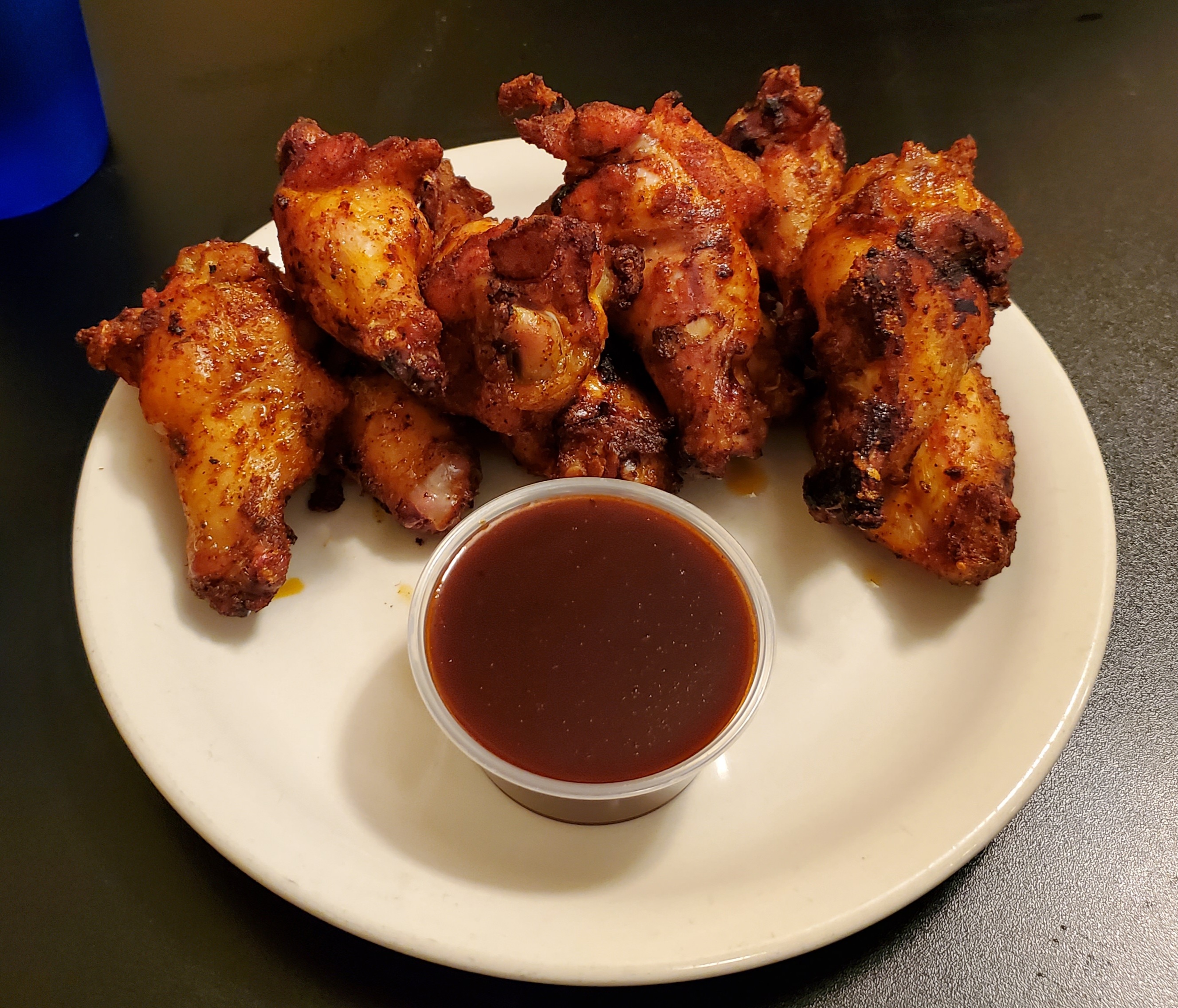 On a white plate, there are six chicken wings arranged in an arch above a cup of sauce. Photo by Carl Busch.