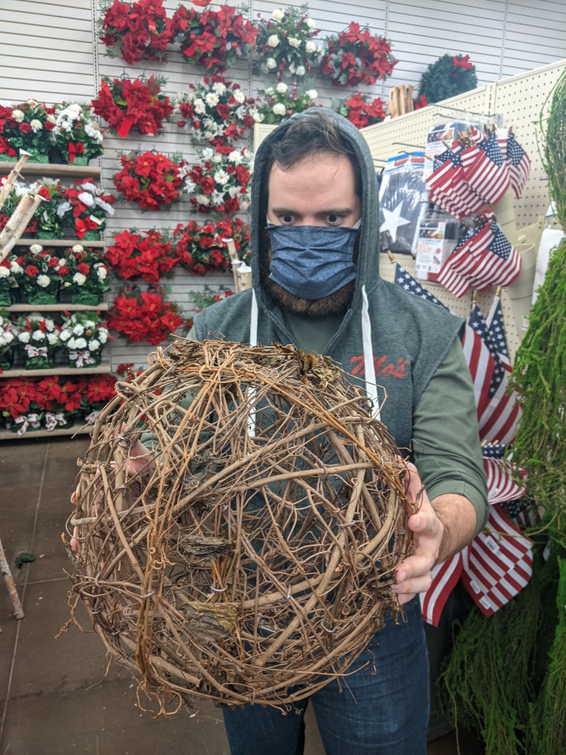 The writer is holding a large ball made of twigs. He is wearing a gray hooded vest with the hood over his head, and he is staring intently at the ball. Photo by Andrea Black.