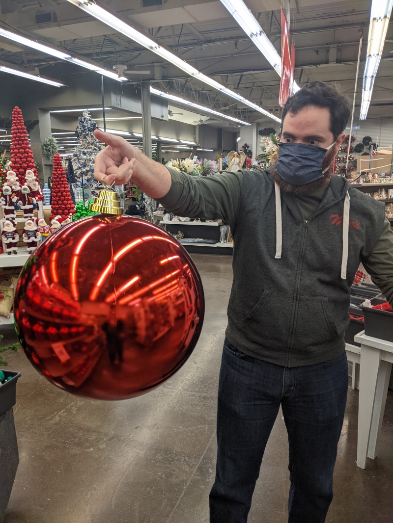 The writer is holding a giant red ball ornament by its hook, and staring at it incredulously. Photo by Andrea Black. 