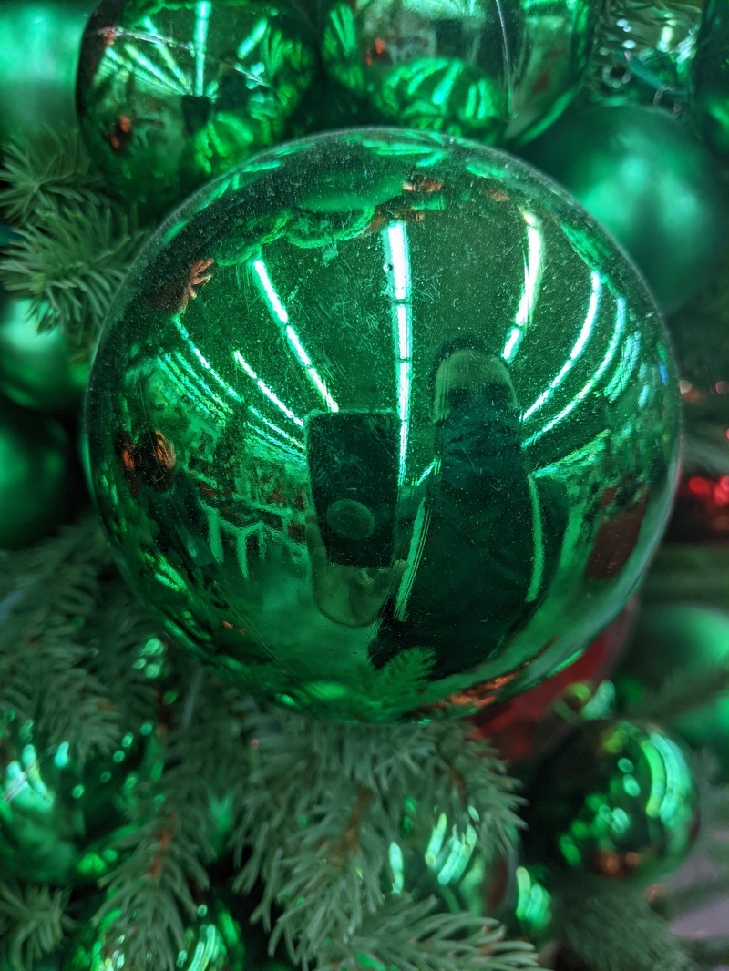 A close up of a shiny green ball ornament. The writer's reflection is in the ornament. Photo by Tom Ackerman.