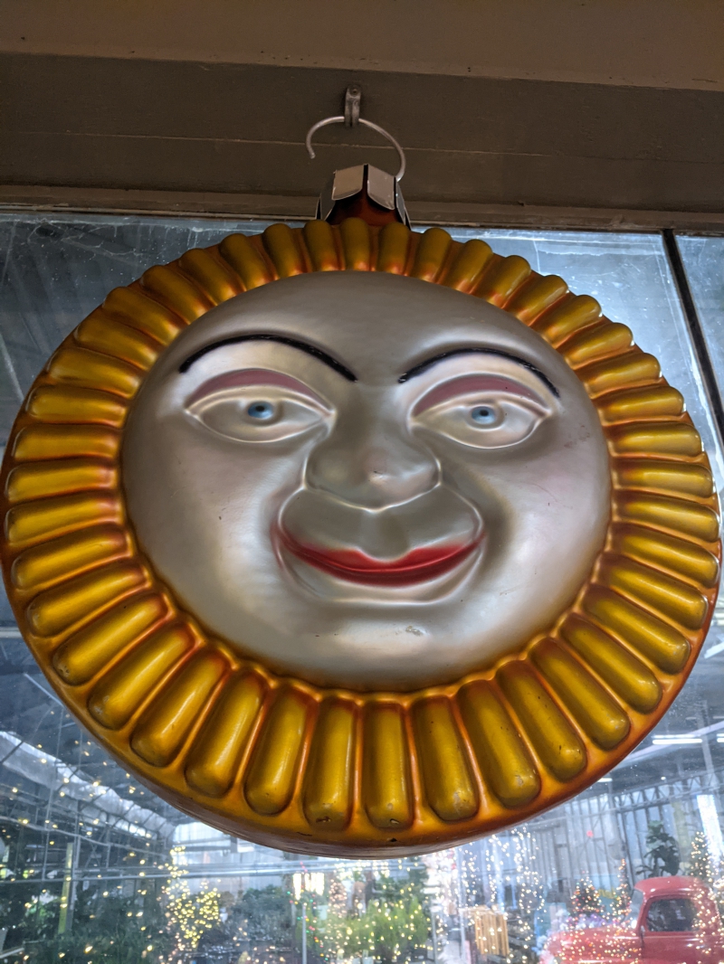 A large round sun decoration that is gold around the outer ring, and has a silver face that seems to be smirking. Photo by Tom Ackerman. 