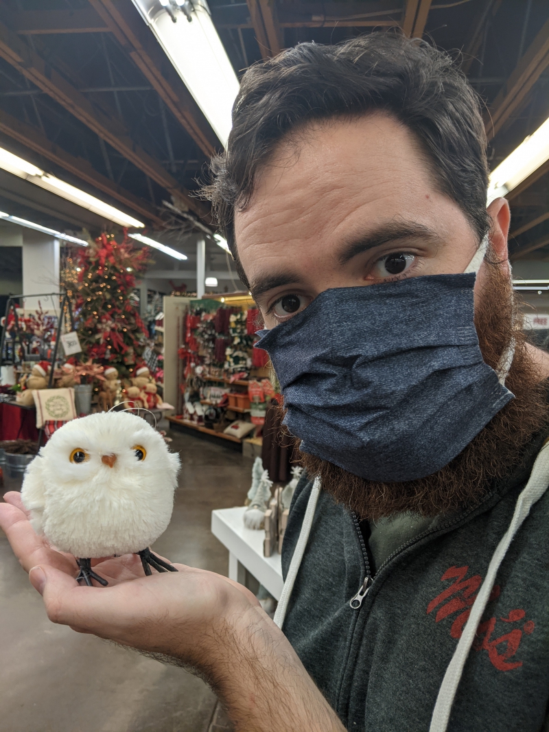 A close up of the writer holding a small, round, white-feathered owl decoration. The owl's eyes are round and open. Photo by Andrea Black. 