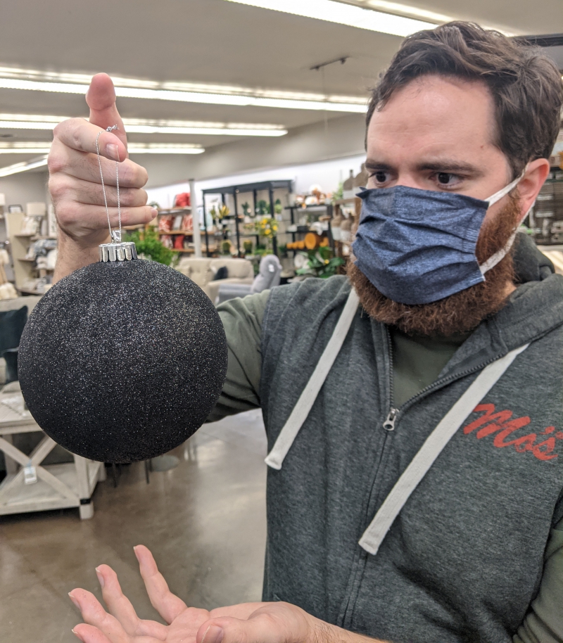 The writer is holding a large black sparkly ball ornament by its hook. He is staring at it and has his other hand open underneath it. Photo by Andrea Black. 