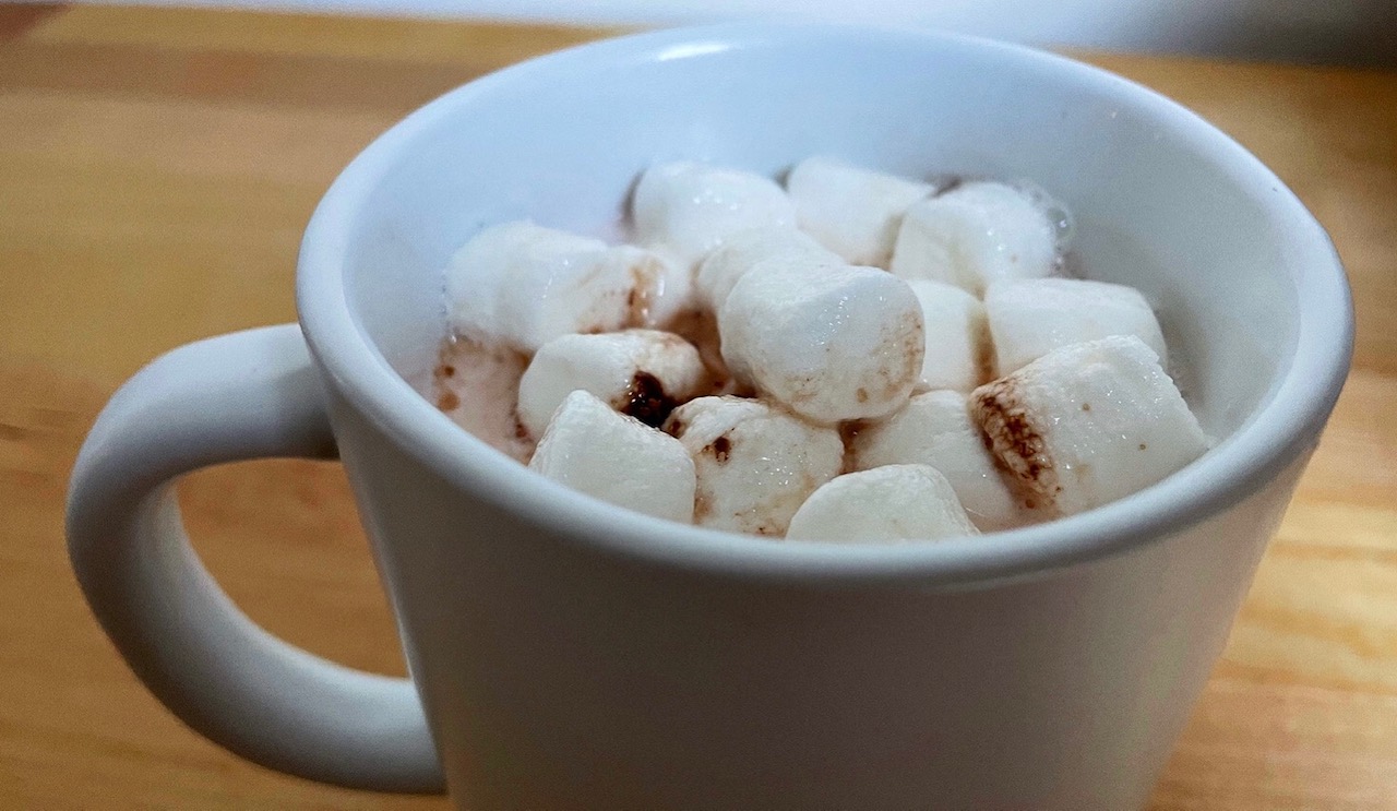 A mug of hot chocolate with lots of mini marshmallows sits on a butcher block counter. Photo by Alyssa Buckley.