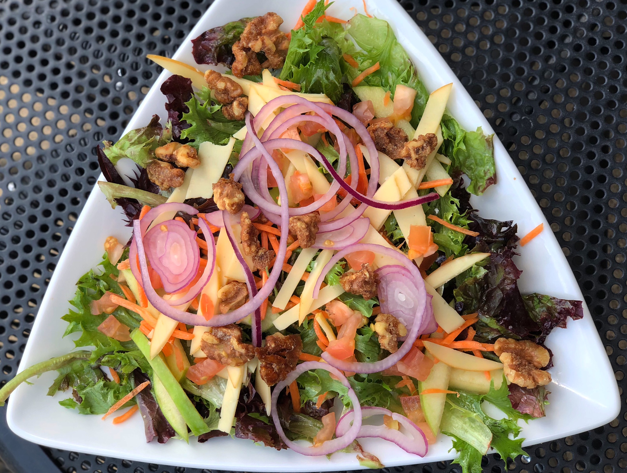 On a white triangular plate, there is a salad with lots of toppings. Photo by Alyssa Buckley.