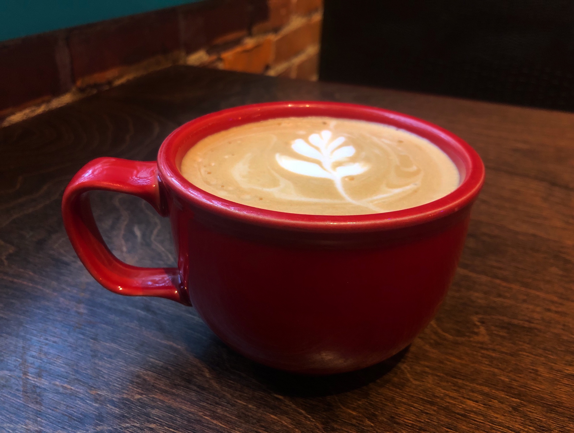 On a brown table, there is a red mug filled with coffee and a pretty latte art. Photo by Alyssa Buckley.