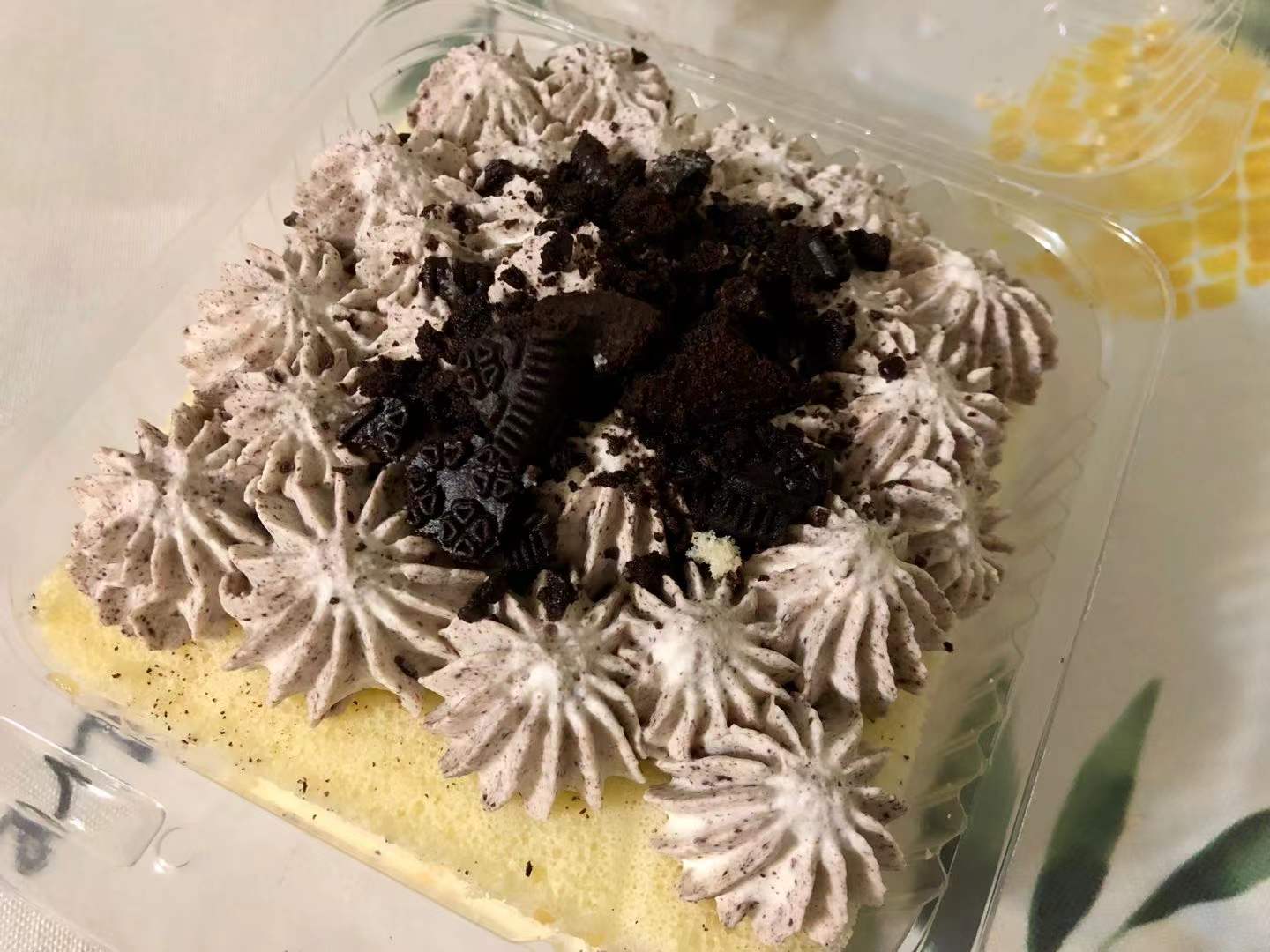 In a plastic takeout container, there is an Oreo cake with lots of poufed gray cream artfully displayed. Photo by Xiaohui Zhang.