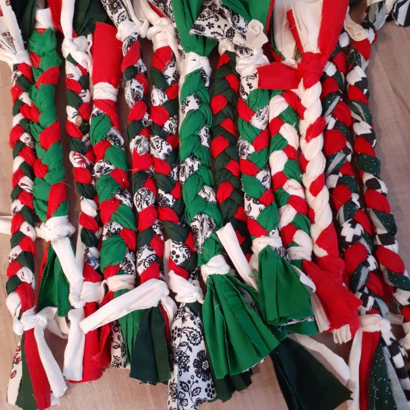 Rope like tug toys are lined up on a table. They are made with red, green, black and white fabrics braided together. Photo from Pura Vida Pets Facebook page.