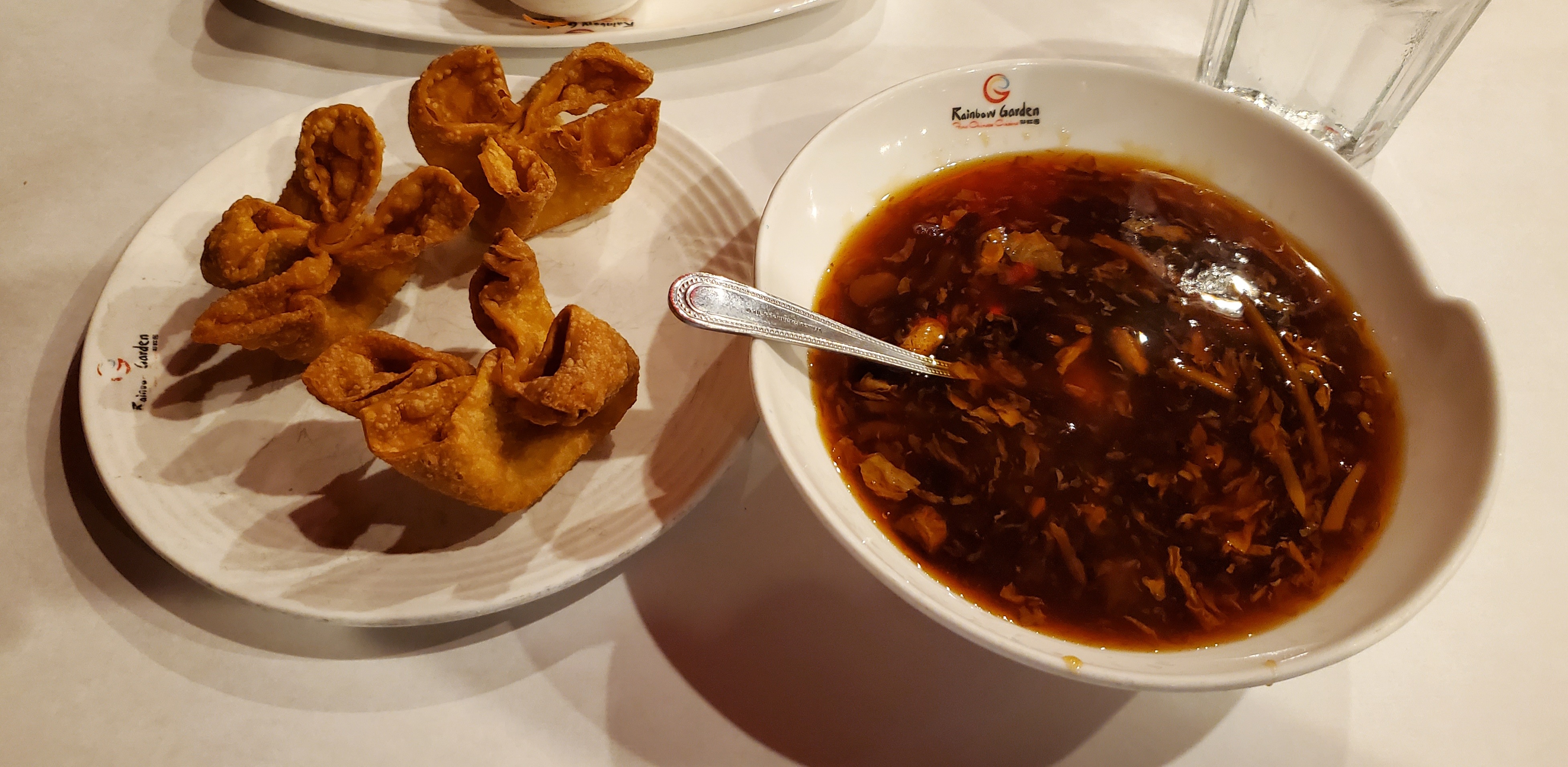 On a white table, there is a plate of crab rangoons and a white bowl of hot and sour soup. Photo by Carl Busch.