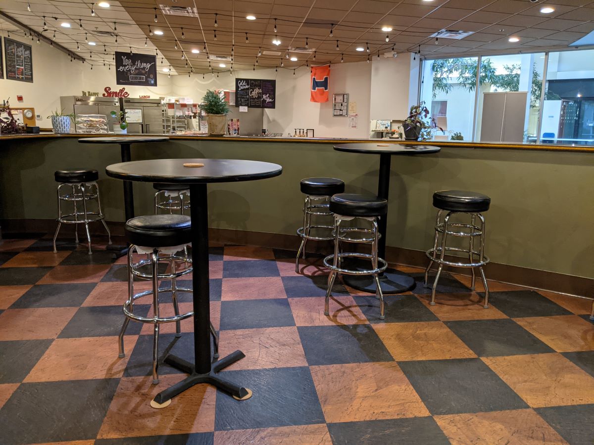 Tall, round tables surrounded by barstools. The floor is checkered black and orange. Photo by Tias Paul.