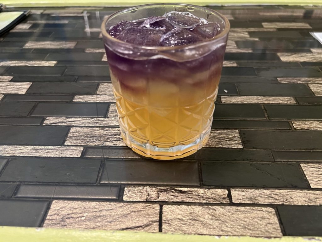A rocks glass with a two-toned drink: the top is purple and the bottom is orange.