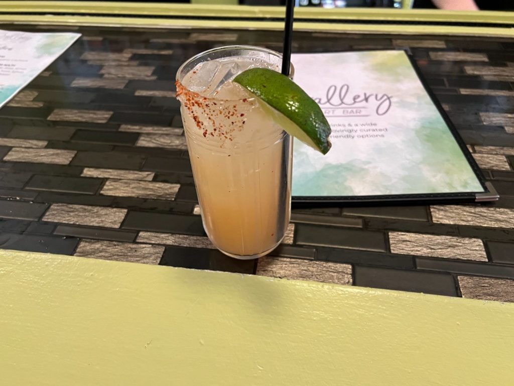 The paloma drink has a light pink-orange liquid with a triangular spread of Tajin beside a lime wedge.