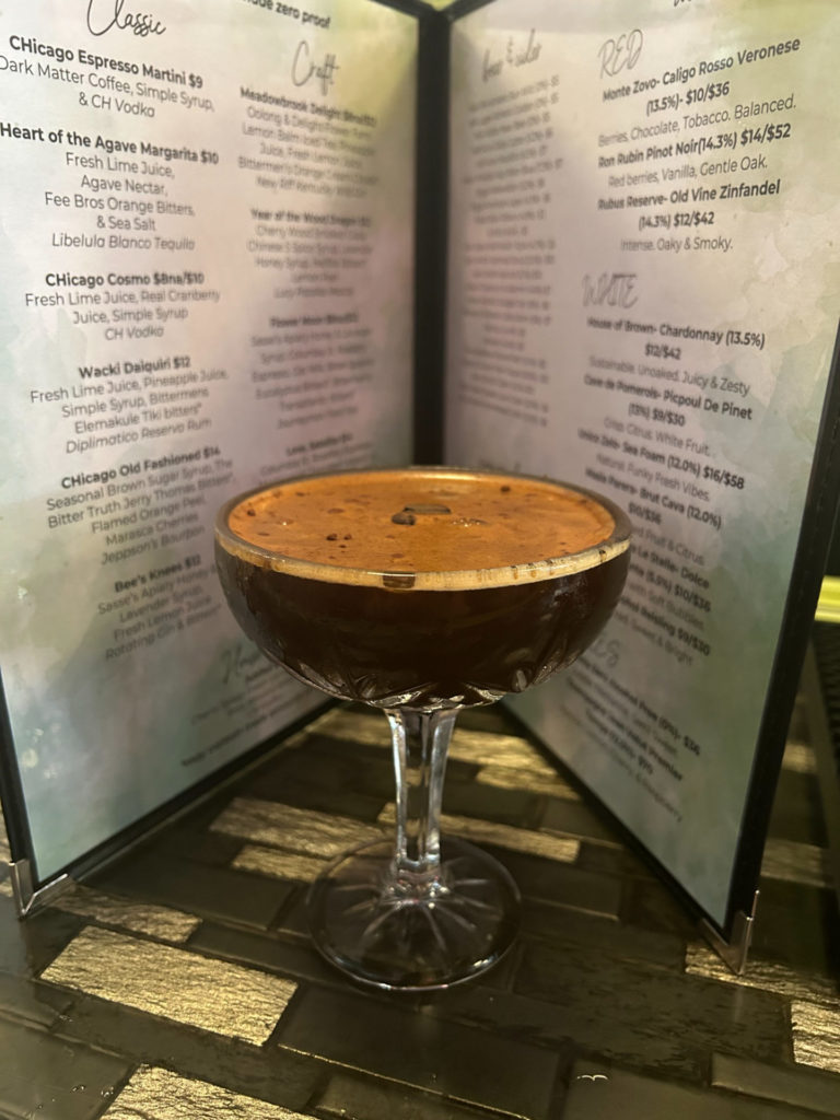 A coupe glass with an espresso cocktail in front of a menu.