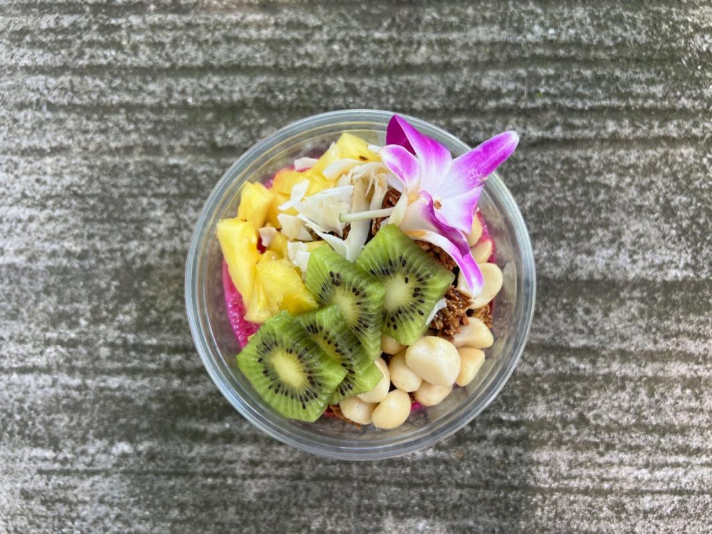A bowl of Açaí with kiwi, pineapple, coconut, macadamia nuts, granola, and an edible flower.