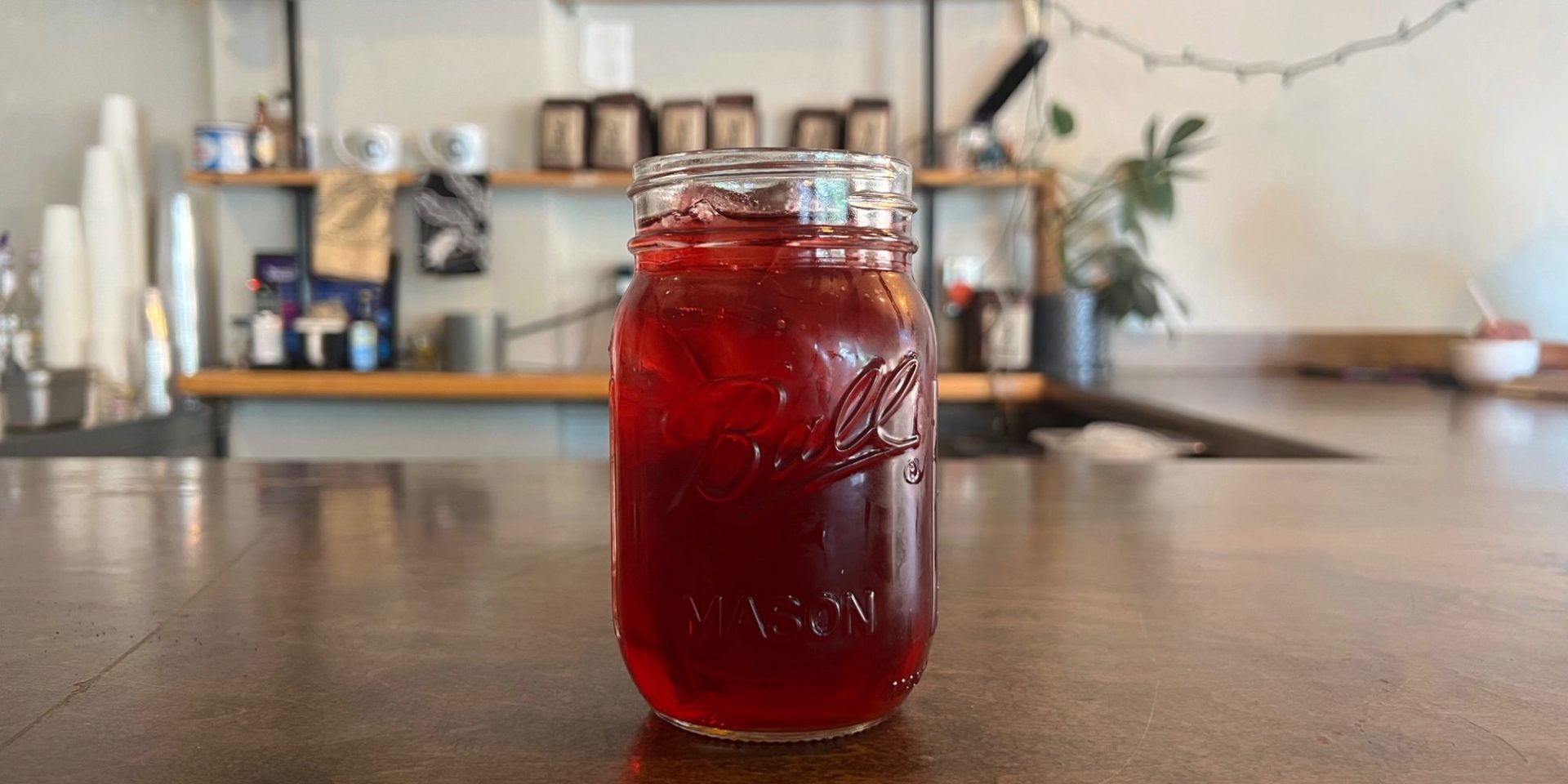 A Ball-brand mason jar with a red liquid and lots of ice on a brown counter inside Avionics in Champaign, Illinois.