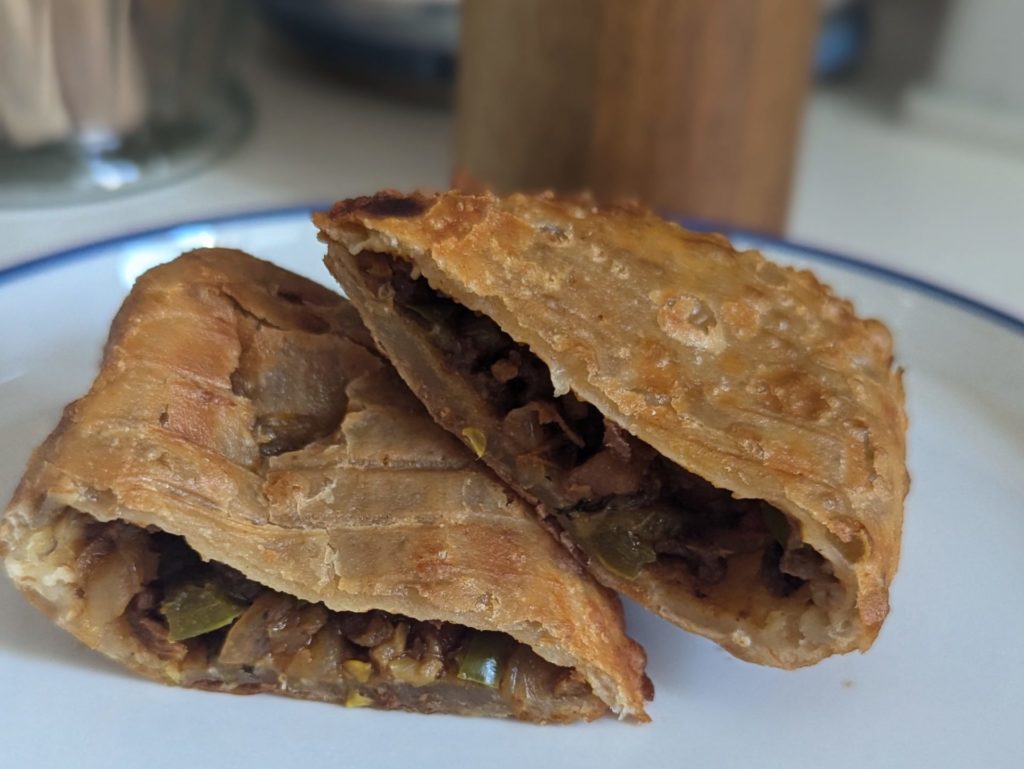 A sliced empanada with brown filling of vegetables.