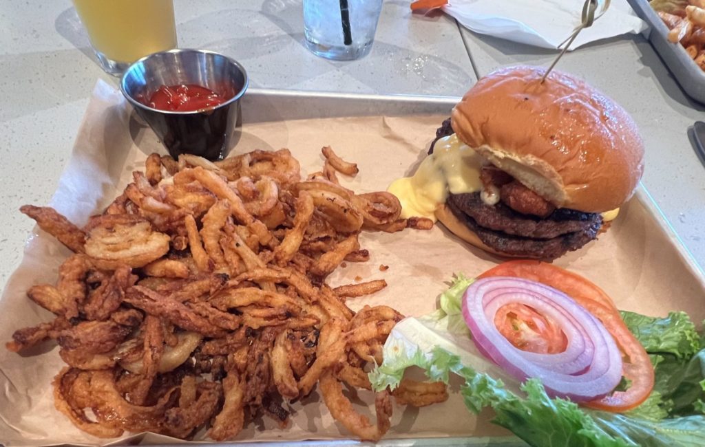 A burger with toppings on the side and a giant portion of crispy onions.