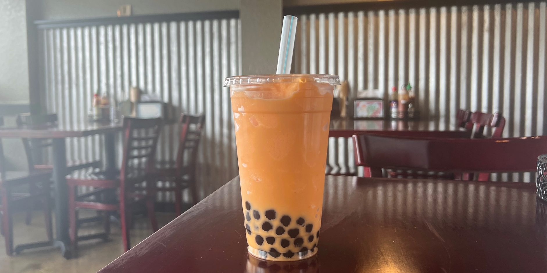 An orange slush with boba on the bottom on a cherry wood table in an empty restaurant.