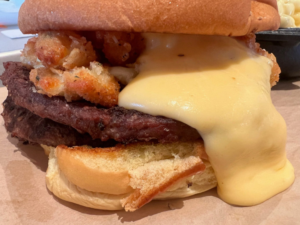 A burger with yellow cheese sauce and beef patties.