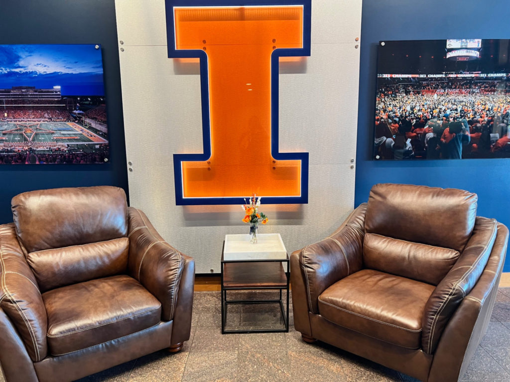 Two brown chairs in front of a wall with a giant "I" for the University of Illinois.