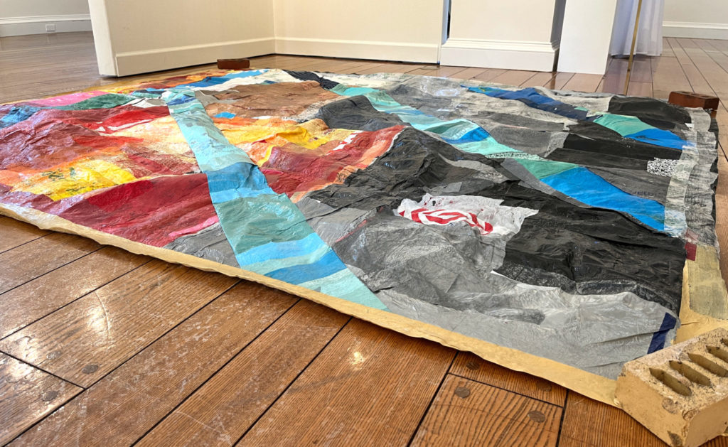 A colorful quilt made of turquoise, red, and orange plastics lies on the ground.