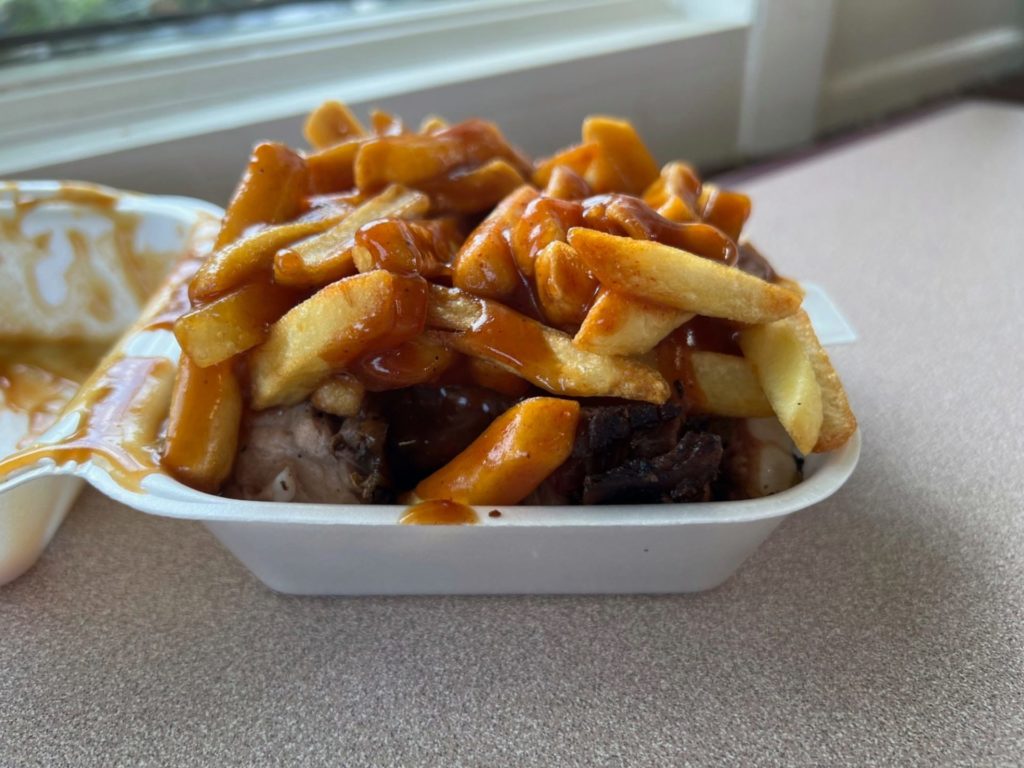 A styrofoam container of jerk rib tips topped with fries and barbecue sauce.