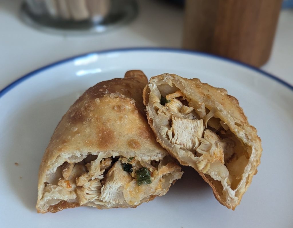 A sliced empanada with cubes of chicken with onions and peppers.