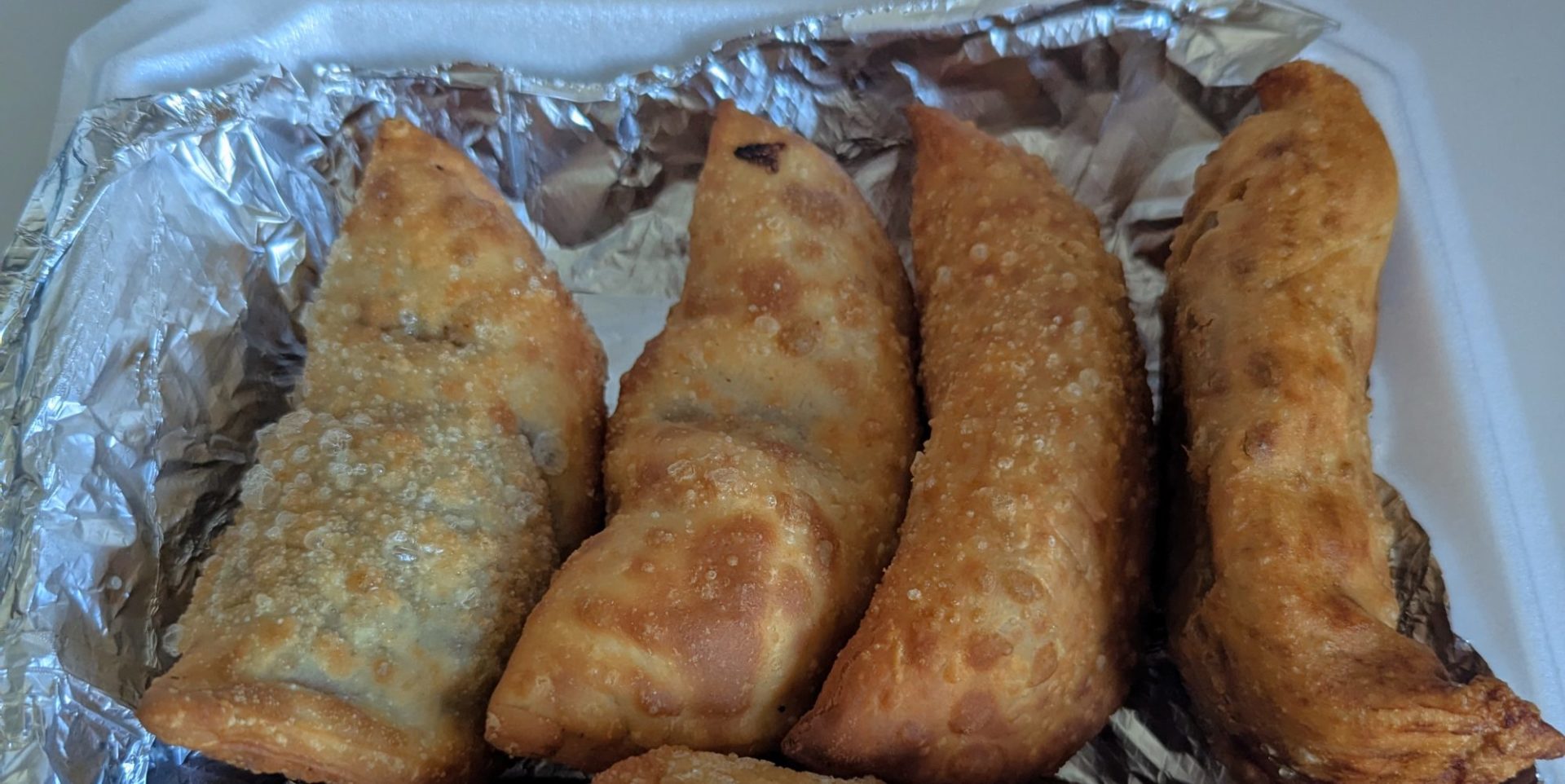 Four fried empanadas in a tin-foil lined box.