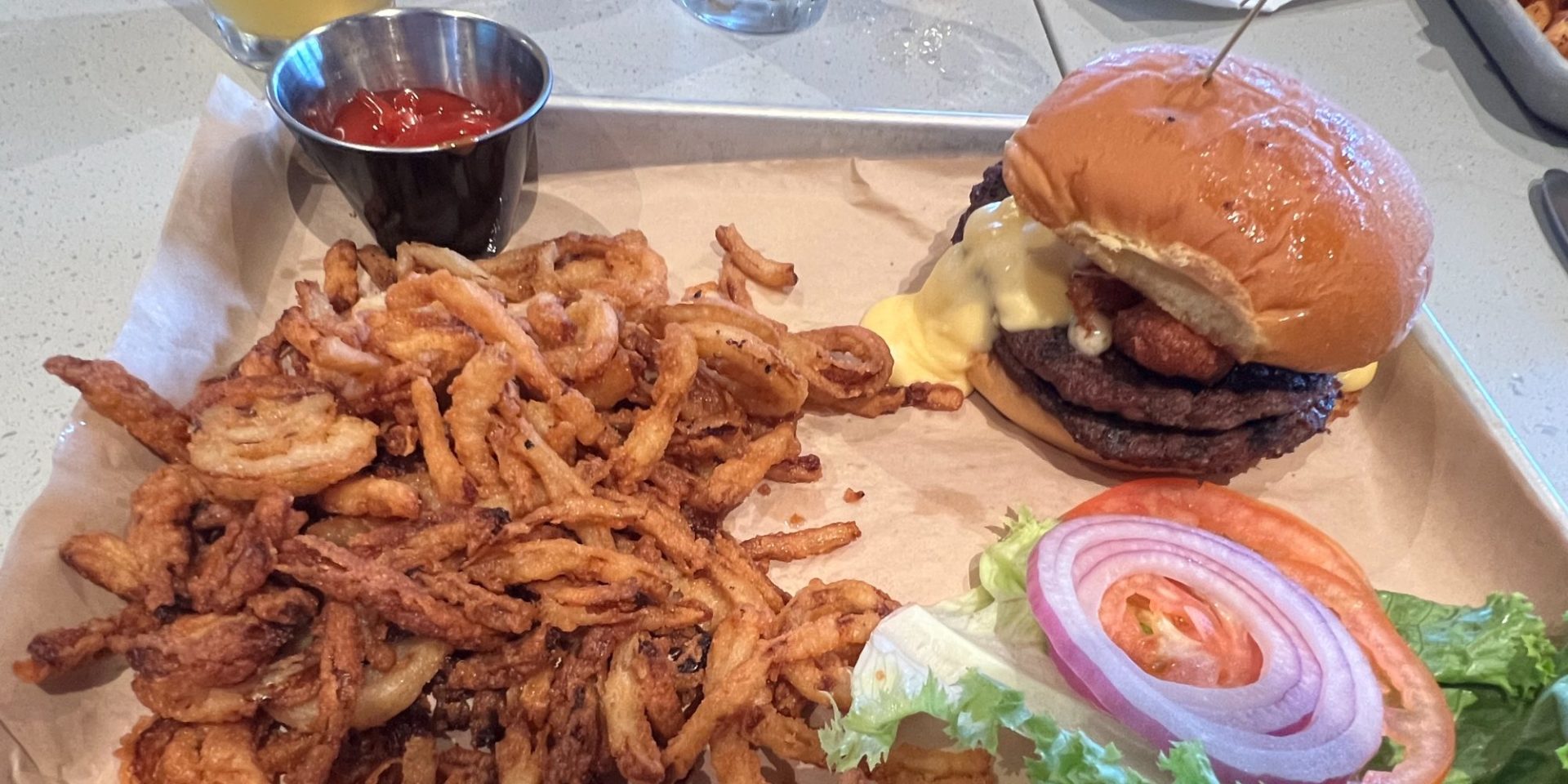 A burger with toppings on the side and a giant portion of crispy onions.